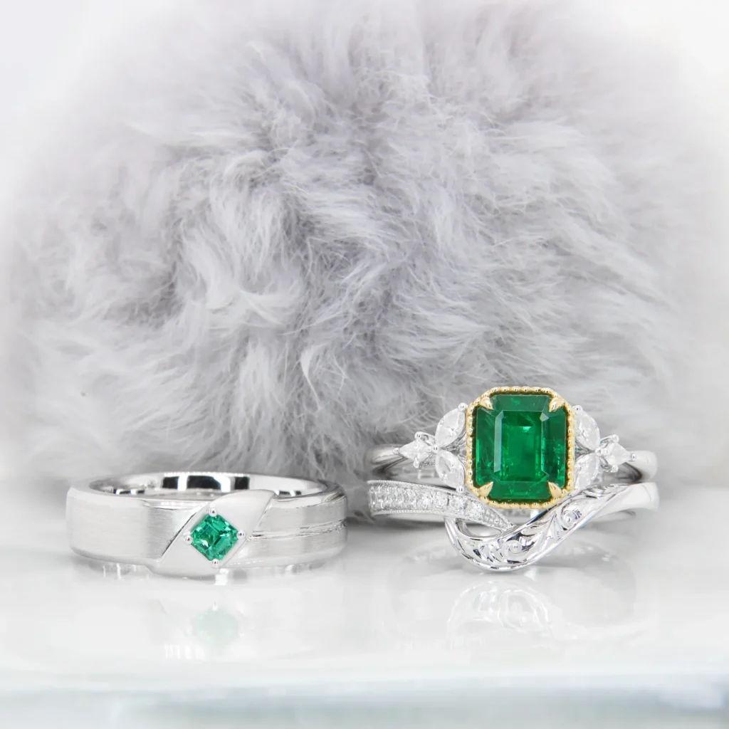 Emerald wedding bands set, men's ring with a bold emerald accent and ladies' filigree wedding band stacked against her emerald proposal ring, GIOIA Singapore