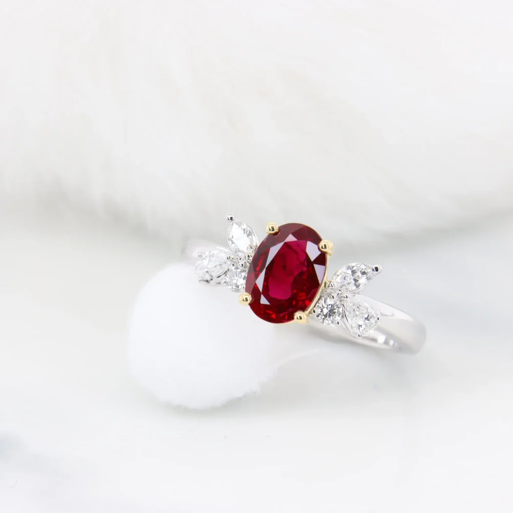 Angled view of the Burma ruby ring showing the diamond clusters fanned out on the white gold shoulders