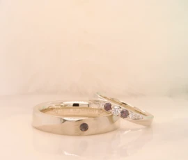 Alexandrite colour change wedding bands in champagne gold under warm light — reddish pink state, men's curved band with flush-set alexandrite and ladies' spiral twist with diamonds, GIOIA Singapore
